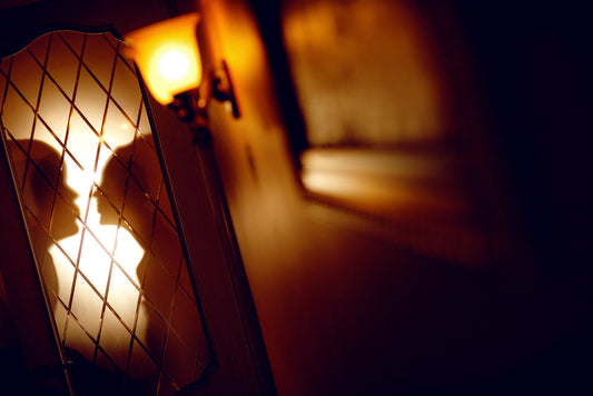 Warm licht dat door een halfopen deur met sierlijk traliewerk valt, in een stille gang vol schaduw en geheimzinnige sfeer.