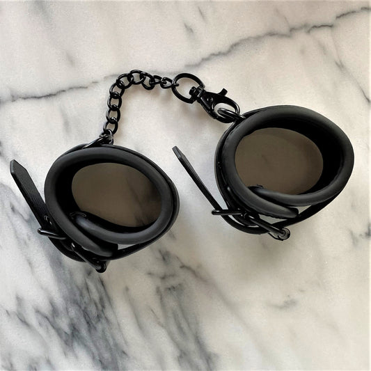 Zwarte vegan leren handboeien verbonden met metalen ketting, bovenaanzicht op marmer