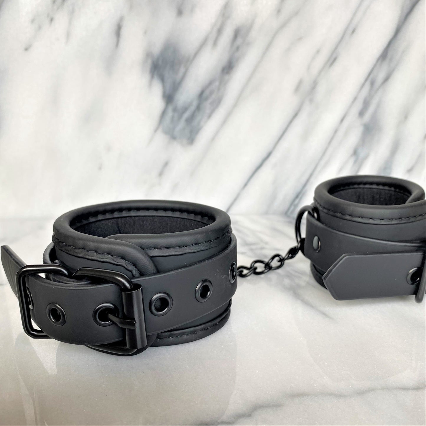 Zwarte vegan leren handboeien close-up met gesp, ketting en zachte voering op marmer