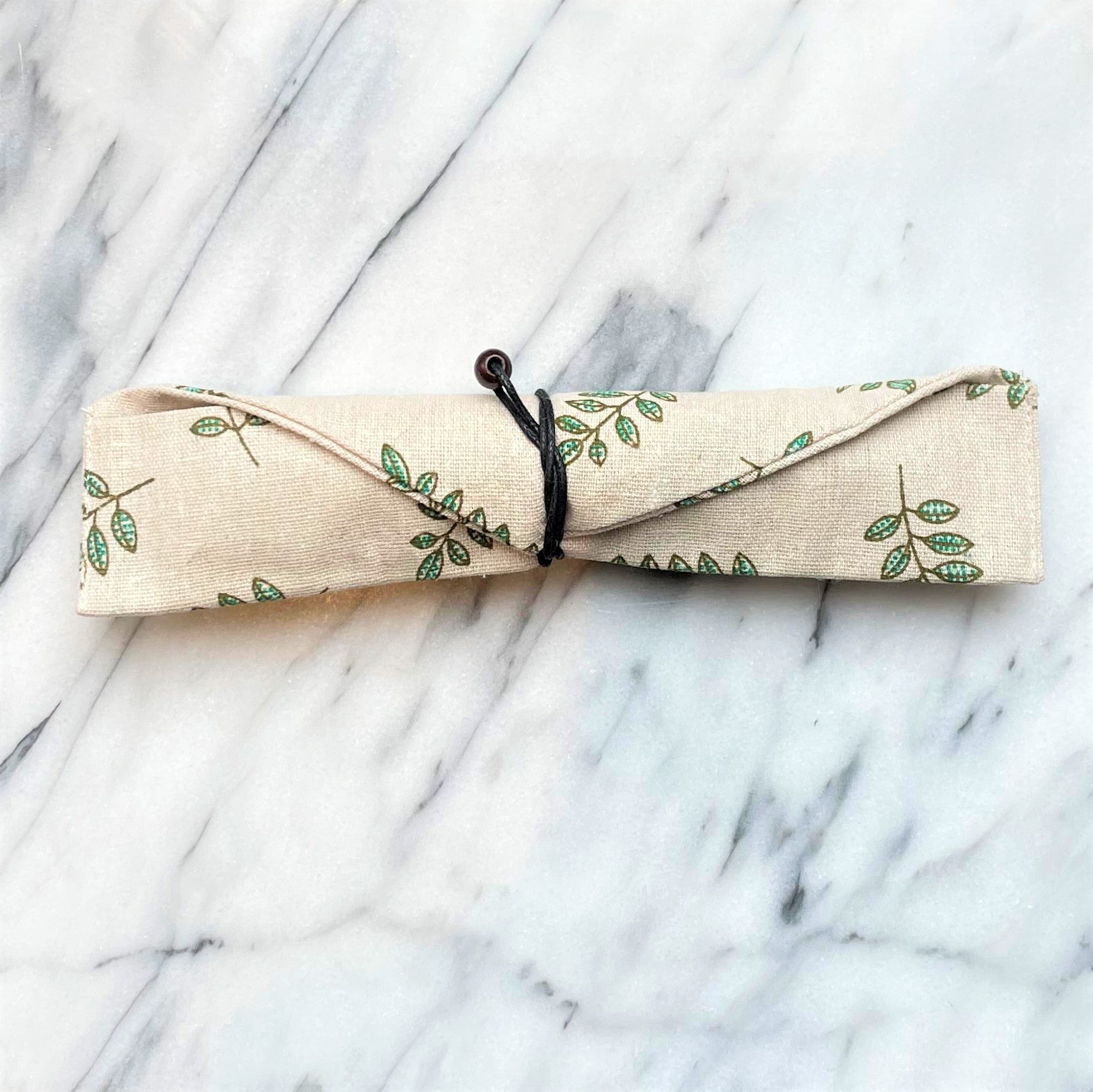 Opgerold beige katoenen etui met groen bladmotief en zwart koord voor rozenkwarts wand